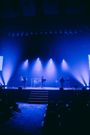 A stage set with bright spotlights and a band tuning instruments before a concert.