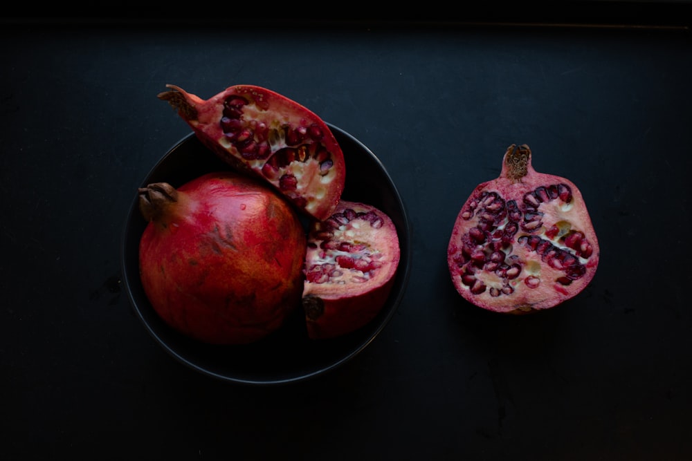 two red pomegranate fruits on black surface