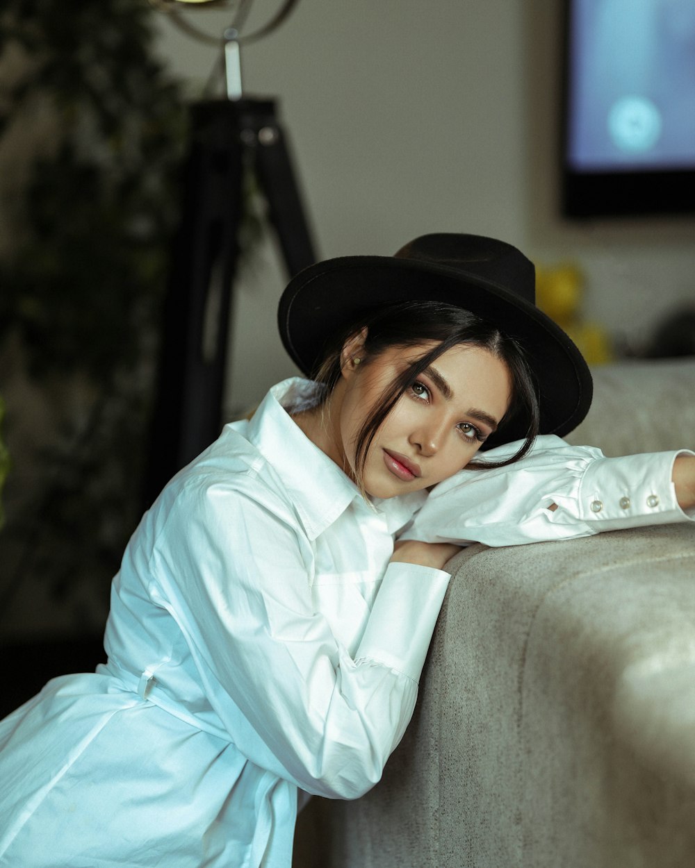 woman in white dress shirt and black fedora hat sitting on gray couch