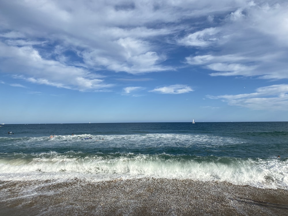 person standing on beach shore under blue sky and white clouds during daytime