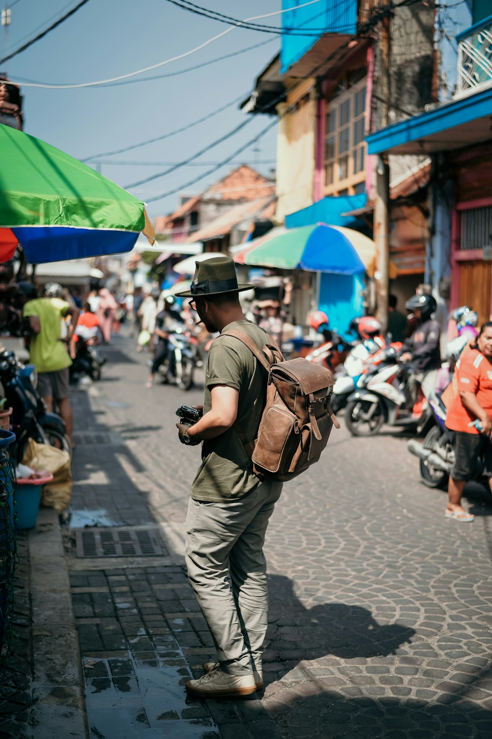 man in brown jacket and black pants with backpack walking on street during daytime