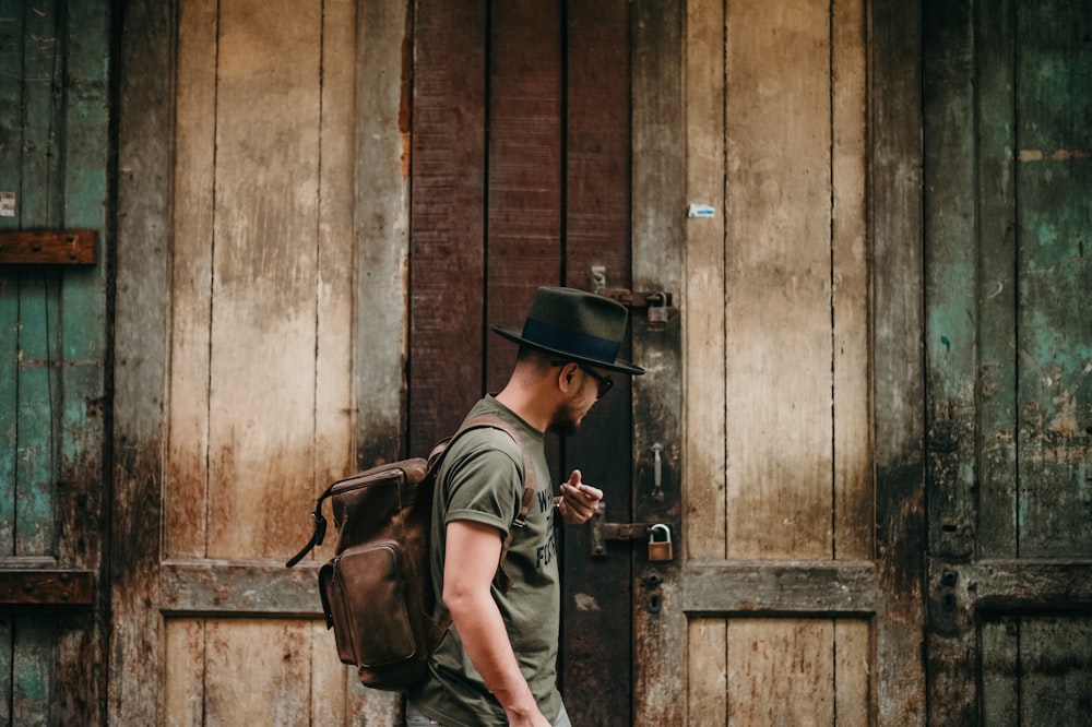 man in black hat and brown backpack standing beside brown wooden door