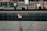 An engraved memorial surface with a small American flag placed in one of the etched names. The background shows a blurred view of people and a construction area.