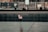An engraved memorial surface with a small American flag placed in one of the etched names. The background shows a blurred view of people and a construction area.