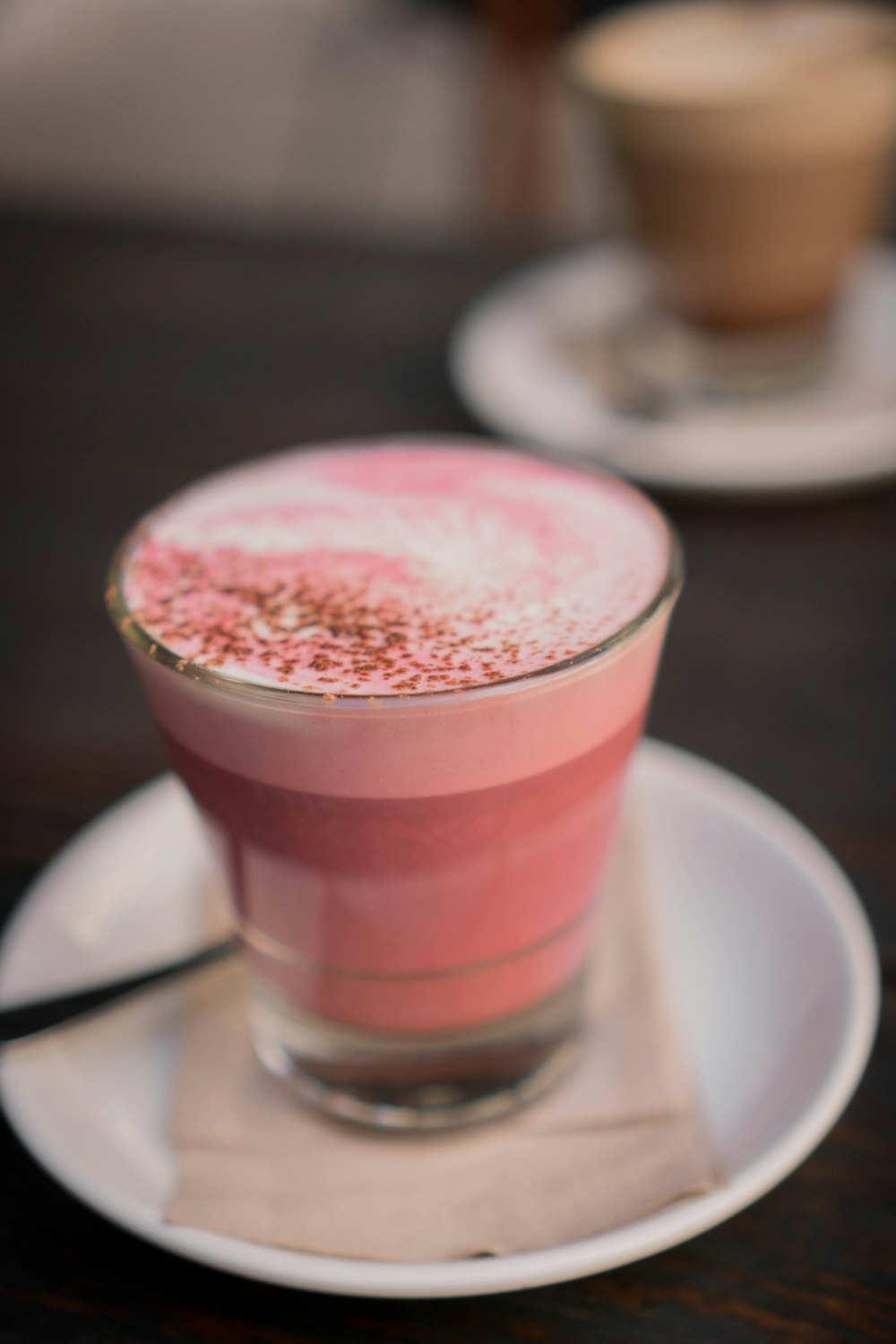 clear drinking glass with pink liquid on white ceramic saucer