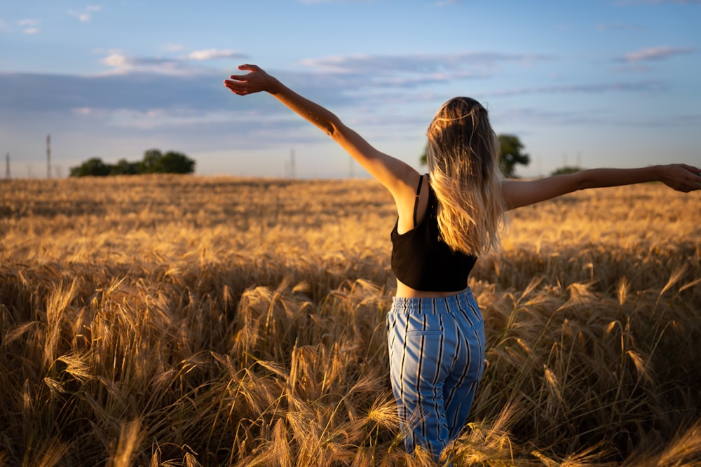 woman in black tank top and blue denim shorts standing on brown grass field during daytime