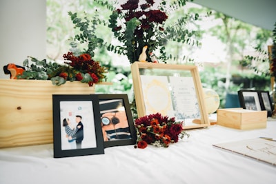 A decorative table display featuring framed photographs, floral arrangements with red and green hues, and documents in wooden frames. A globe and other decorative elements are present, creating an elegant and celebratory ambiance.