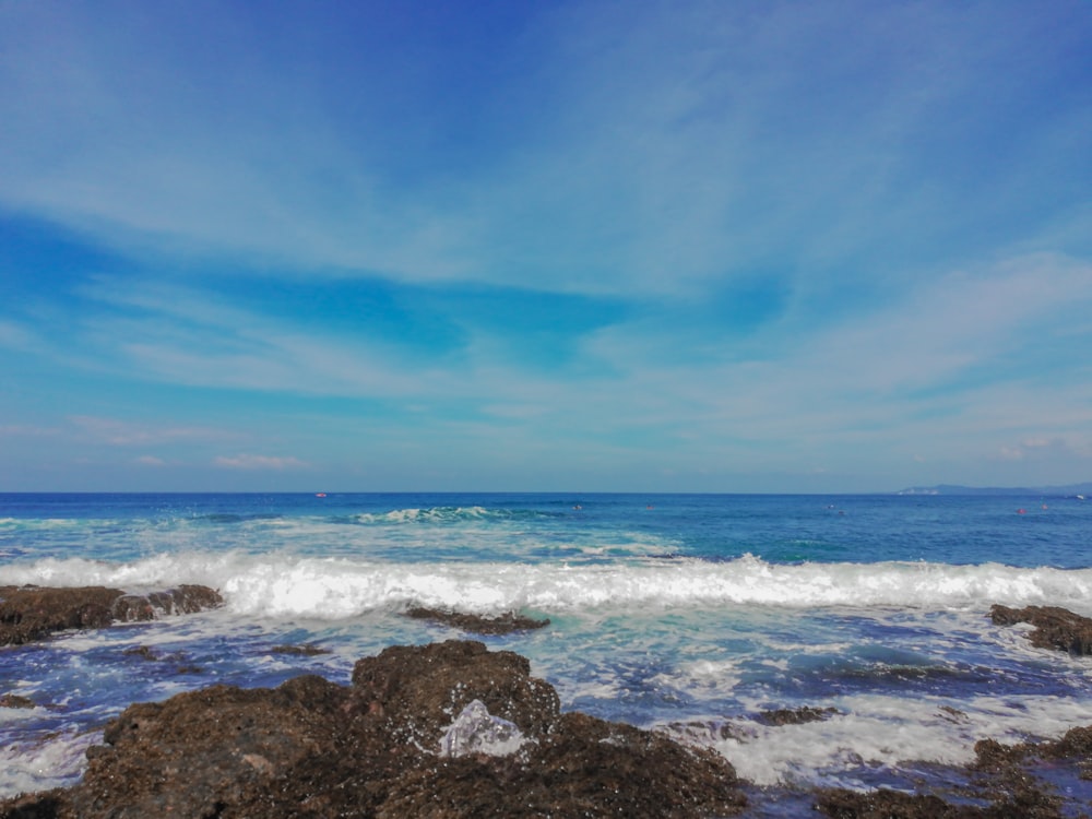 ocean waves crashing on rocks under blue sky during daytime