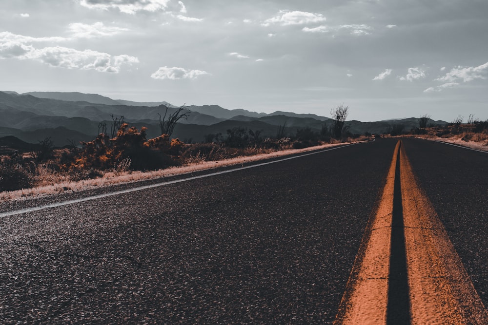 black asphalt road between brown grass field under white cloudy sky during daytime