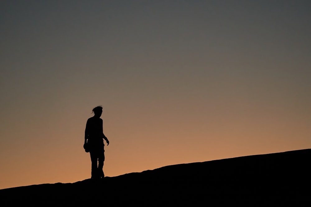 silhouette of man standing on hill during sunset