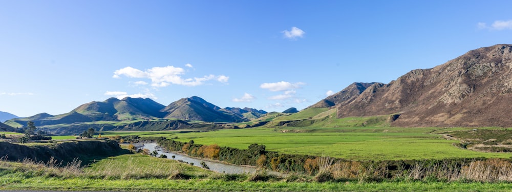 green grass field near mountain under blue sky during daytime