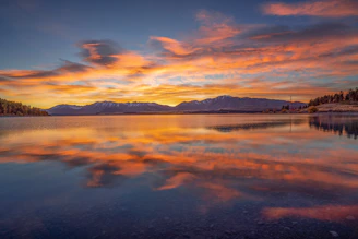 A serene landscape showing a calm lake reflecting a colorful sunset.