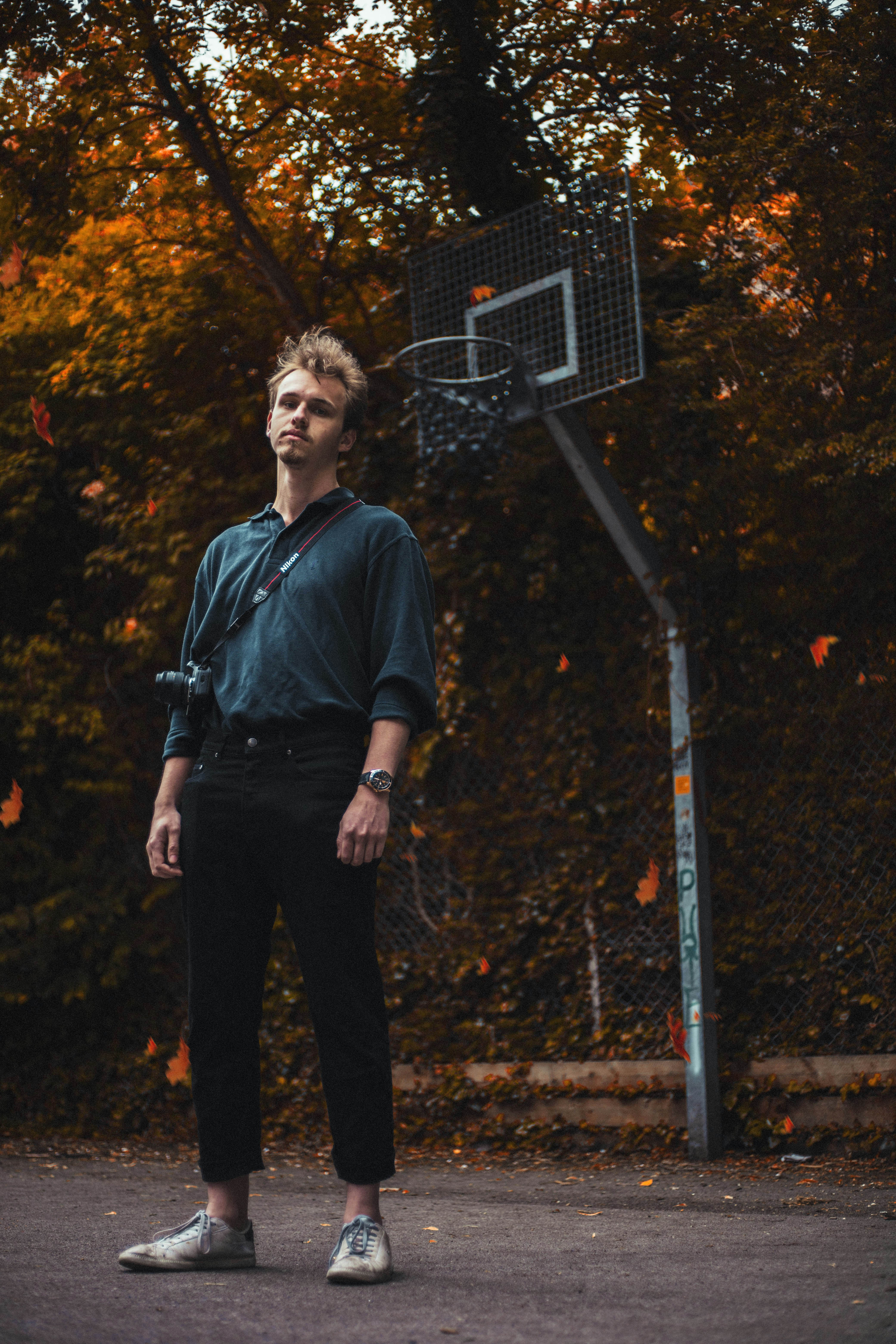Homme en chemise noire et pantalon noir debout près des arbres