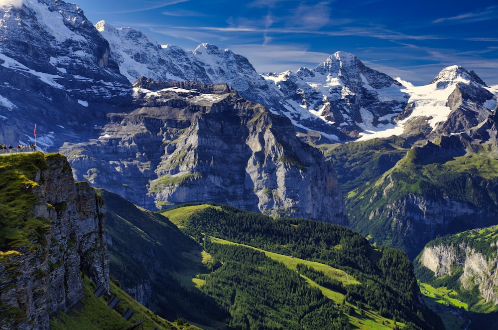 green grass field near snow covered mountain under blue sky during daytime