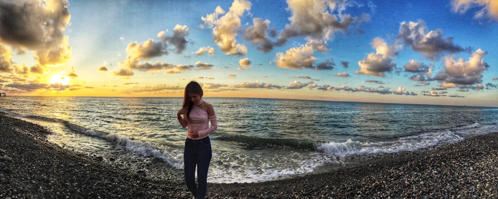 woman in pink tank top and black pants standing on rocky shore during daytime