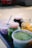 Several jars and containers filled with different colored foods, placed on a surface. The jars contain green, yellow, and purple ingredients with visible spoons for serving.