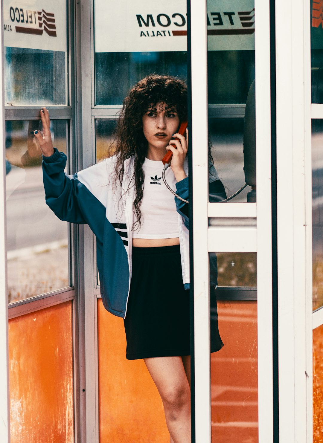 woman in white jacket and blue skirt standing beside glass window