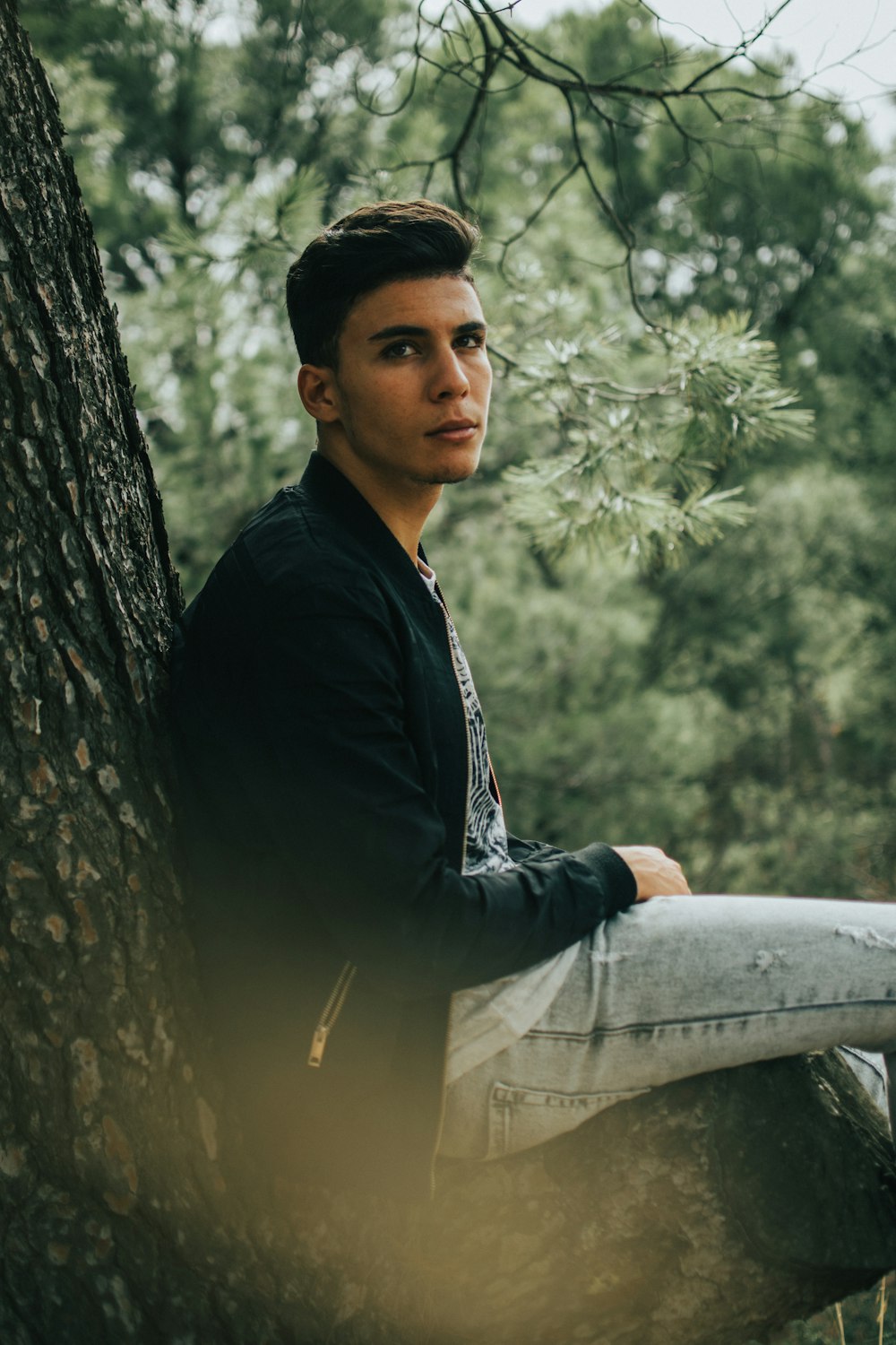 man in black dress shirt and blue denim jeans sitting on tree