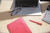 Close-up of a calculator and notebook on a wooden desk.