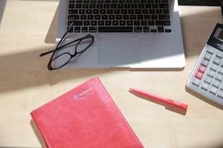 Close-up of hands using a calculator and laptop on a desk