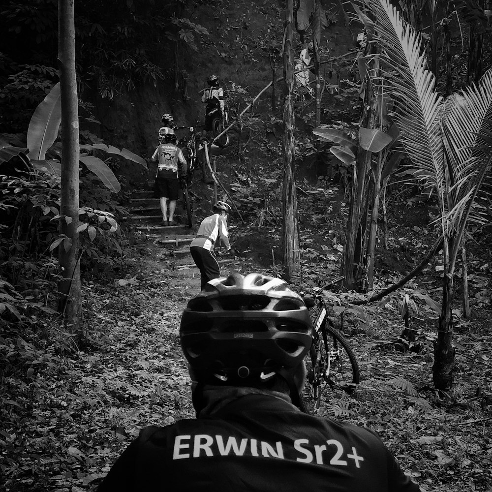 grayscale photo of man riding bicycle in forest