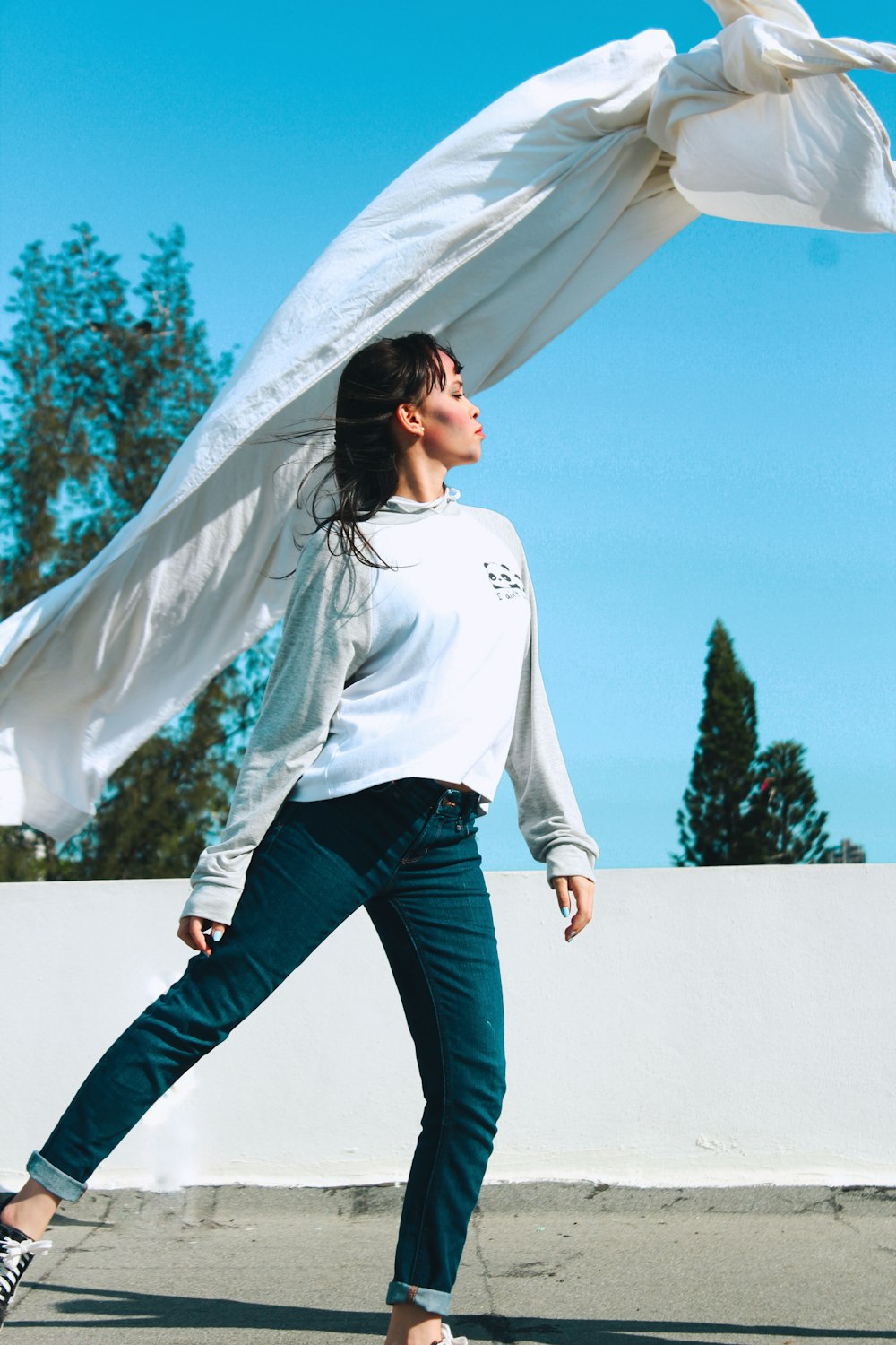 woman in white long sleeve shirt and blue denim jeans standing on white sand during daytime