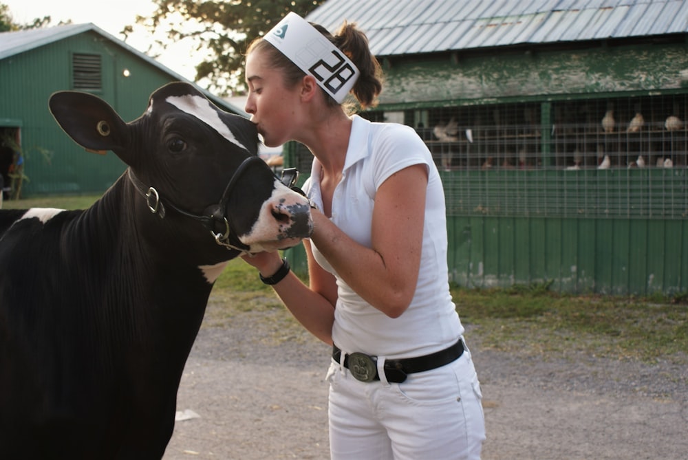 woman in white t-shirt and white pants standing beside black horse during daytime