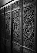 Elaborately carved wooden panels with intricate patterns and decorative motifs, showcasing traditional craftsmanship. The panels are made with detailed designs and feature artistic scenes inside ornate frames.