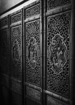 Elaborately carved wooden panels with intricate patterns and decorative motifs, showcasing traditional craftsmanship. The panels are made with detailed designs and feature artistic scenes inside ornate frames.