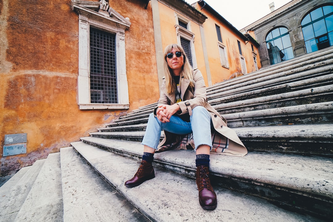 woman in brown coat and blue denim jeans sitting on stairs