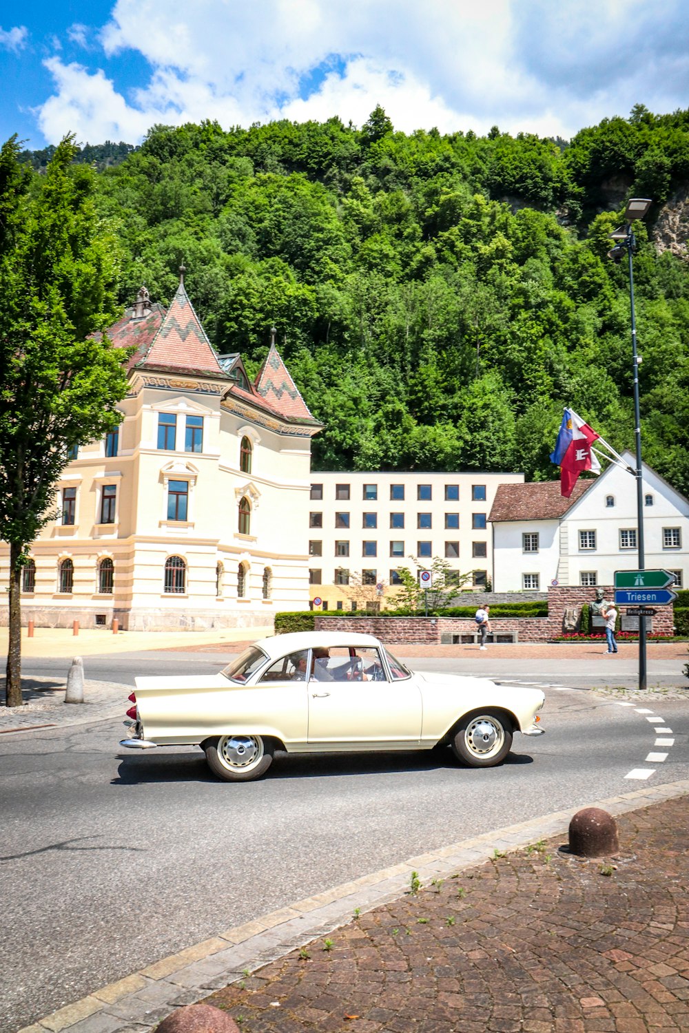 white sedan on road near green trees and buildings during daytime