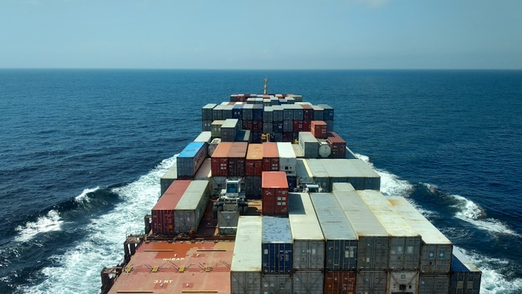 A cargo ship loaded with scrap metal containers sailing from Australia to India under a clear blue sky.