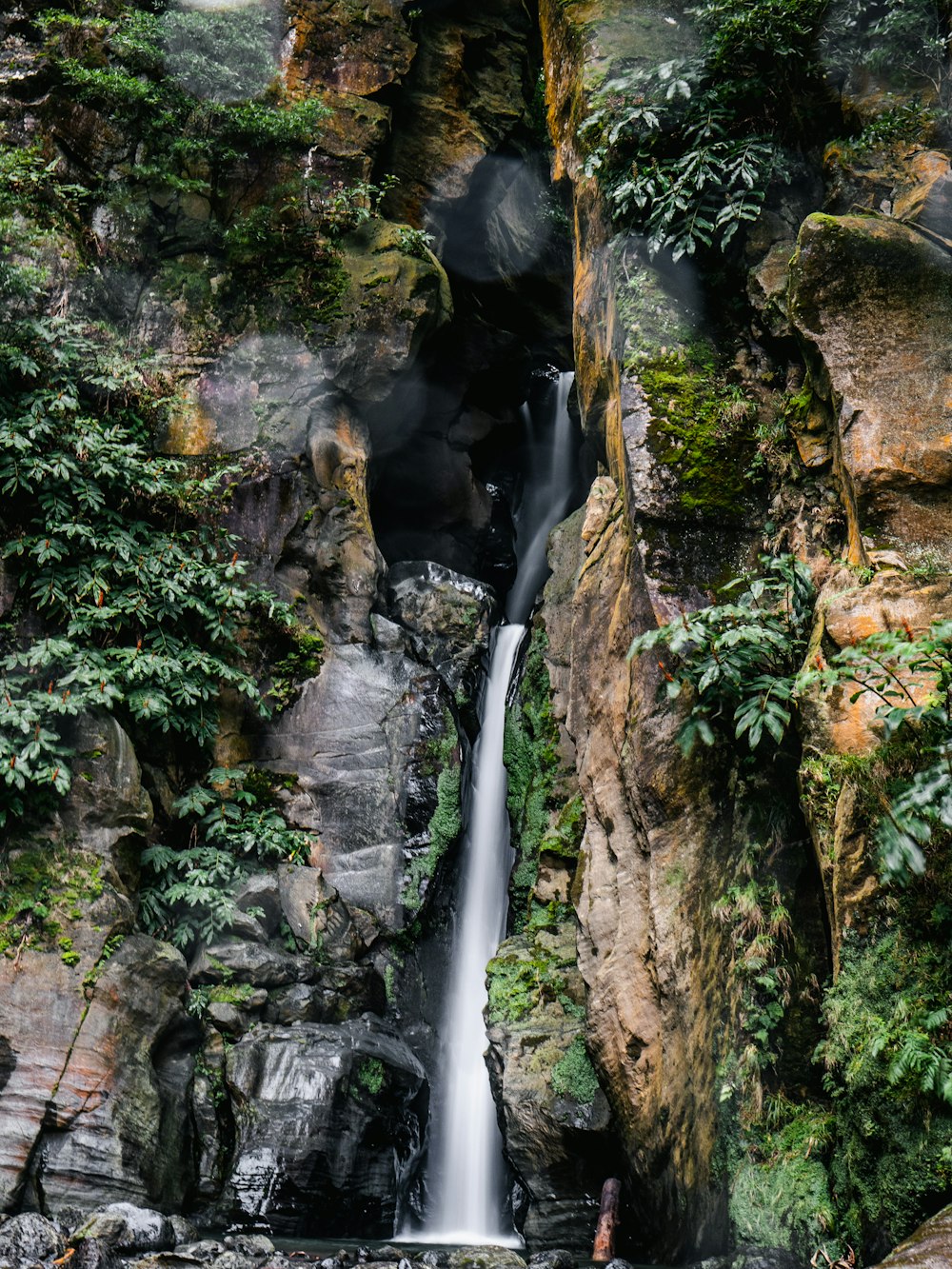 waterfalls between brown and green rock formation during daytime