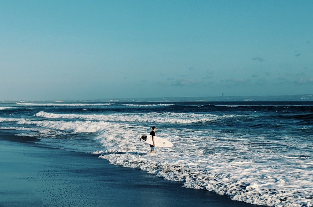 una persona che tiene una tavola da surf che cammina nell'oceano