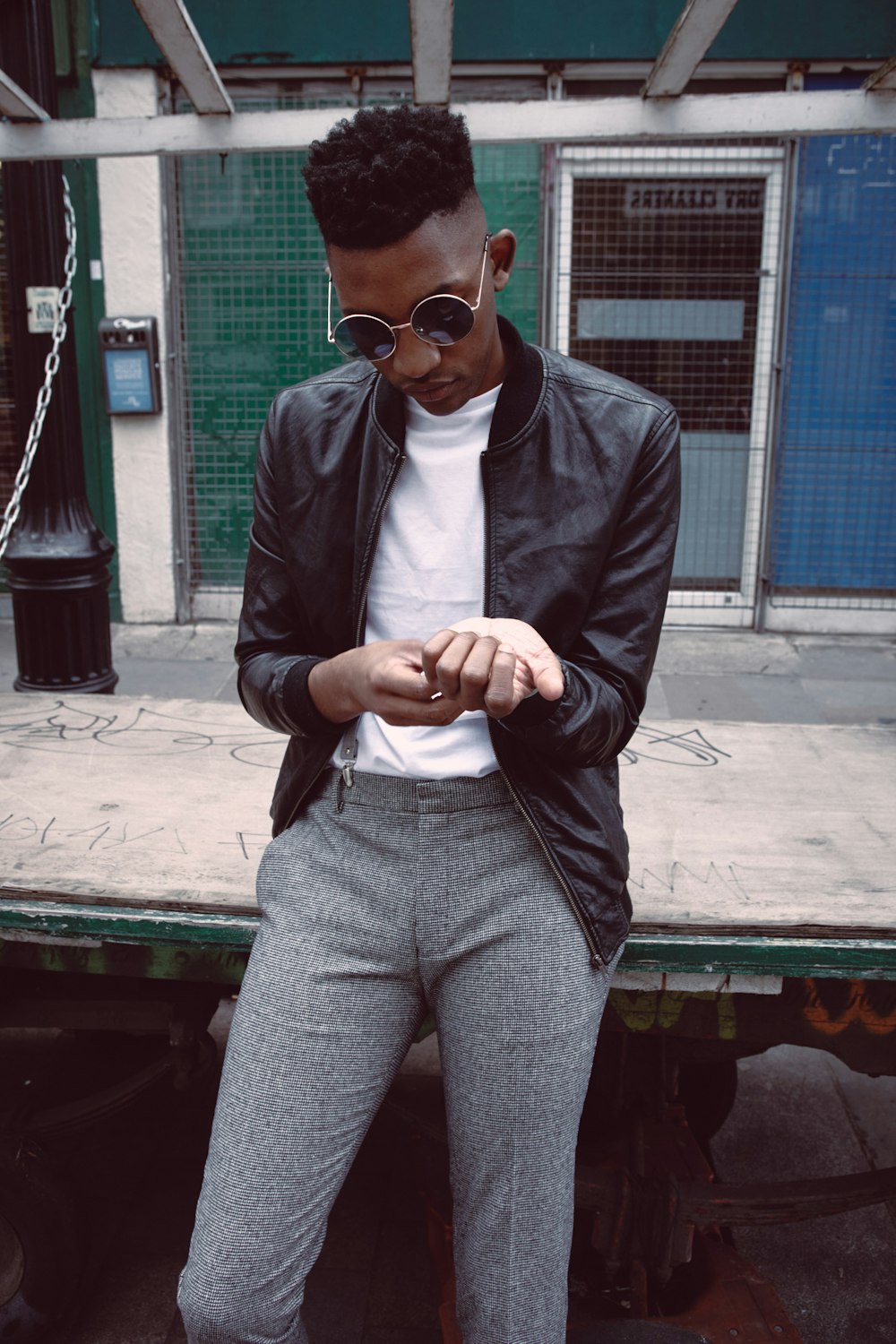 man in black leather jacket and gray pants sitting on green wooden bench during daytime