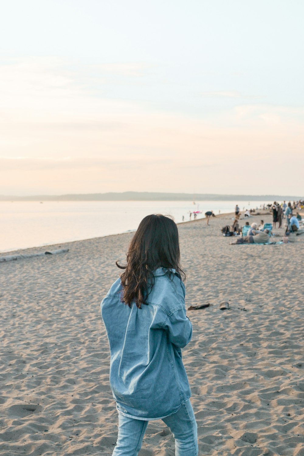 woman in blue denim jacket walking on beach during daytime