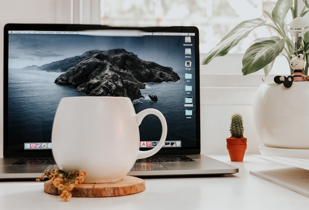 macbook pro beside white ceramic mug on brown wooden table