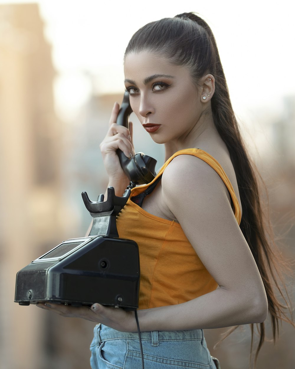 woman in orange tank top holding black telephone