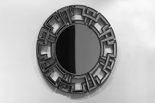 Miroir rond avec cadre noir aux motifs géométriques.