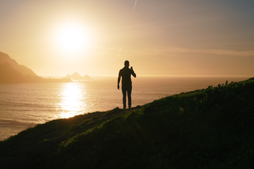 silhouette of man and woman standing on grass field near body of water during daytime