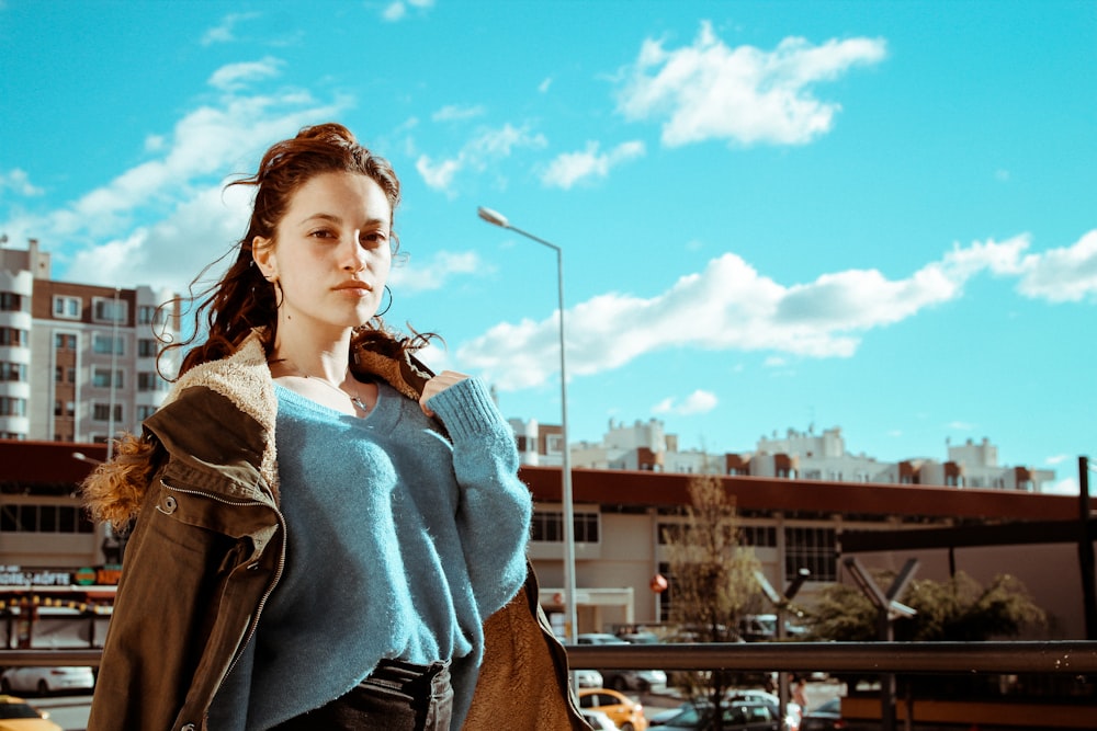 woman in blue and brown jacket holding black smartphone during daytime