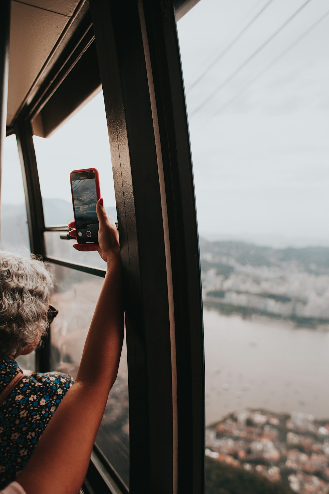 woman in blue and white floral shirt holding red smartphone