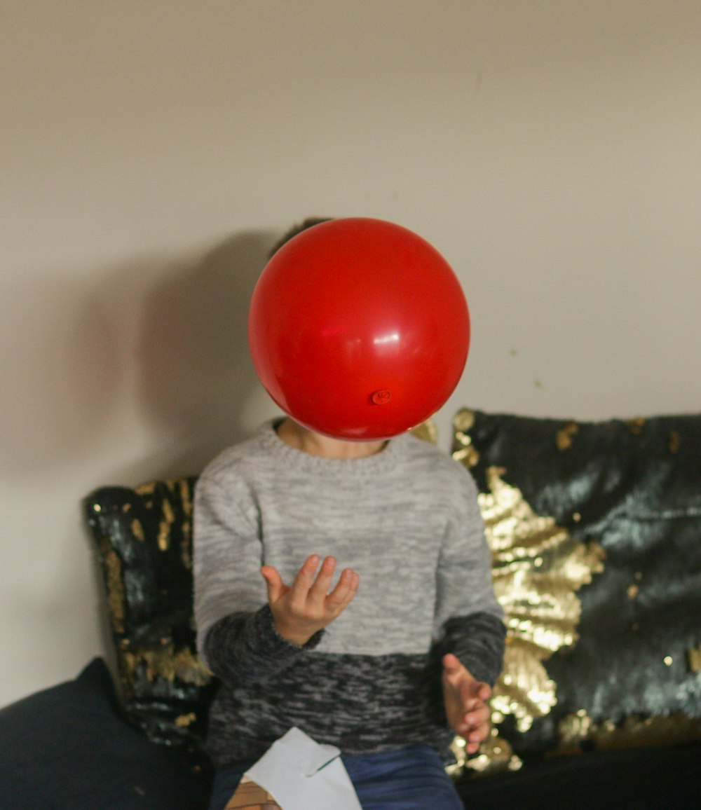 boy in gray and black sweater holding red ball