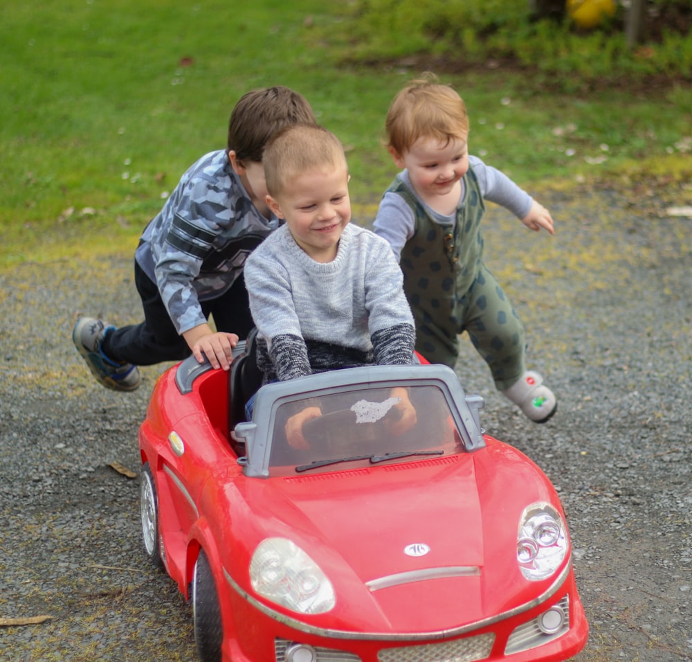 灰色のパーカーを着た男の子がおもちゃの車に乗って赤い乗り物に乗る