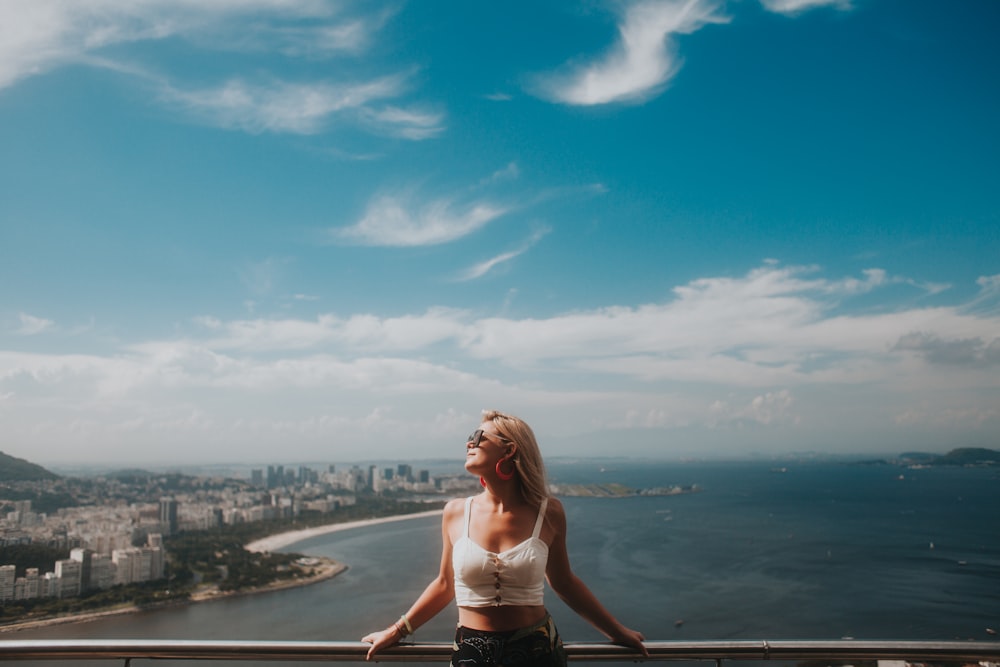 Frau im weißen Bikini steht am Rand eines Gebäudes und blickt auf das Meer während