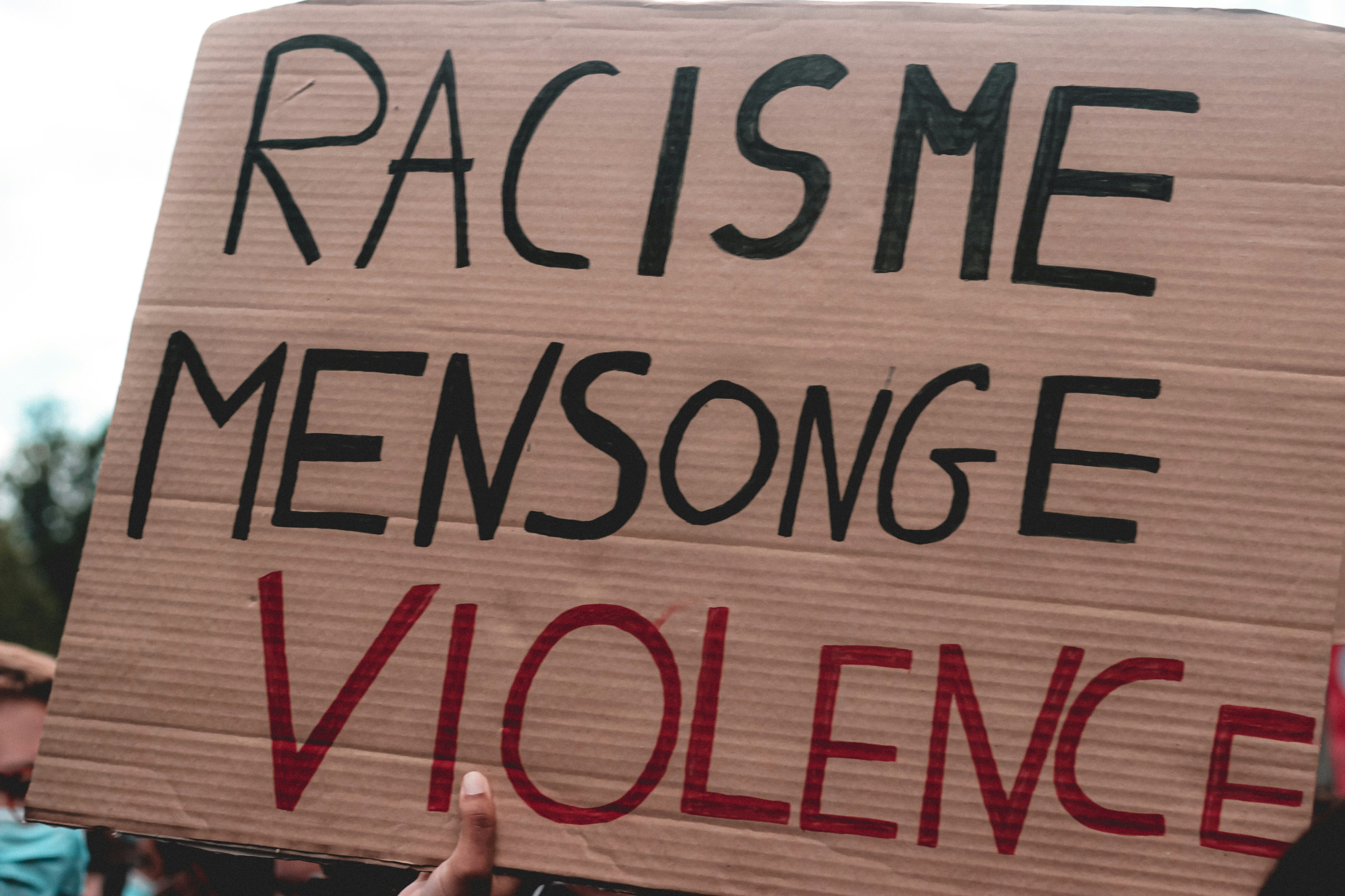 a person holding a sign that says racisme mensonge violence (Photo by Mathias Reding on Unsplash)