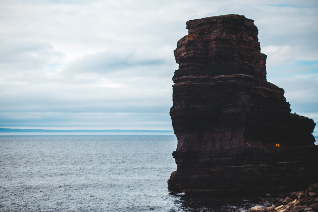 brown rock formation on sea under white clouds during daytime