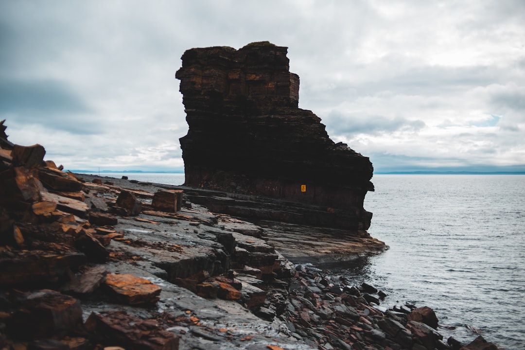 brown rock formation on sea under white clouds during daytime