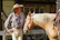 Smiling customer wearing a cowboy hat and boots, standing in a sunlit barn.