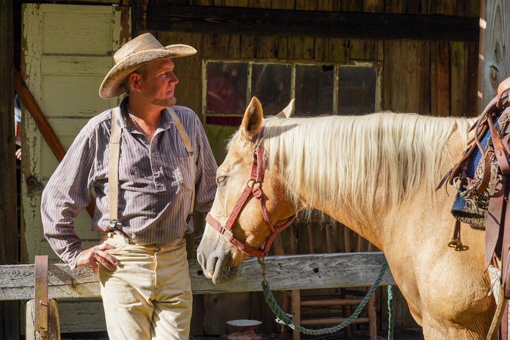 man in blue and white button up shirt and brown pants standing beside brown horse during